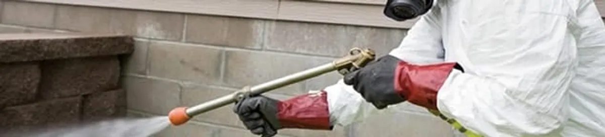 Pest control technician applying exterior insect treatment along a home foundation in Akron, OH
