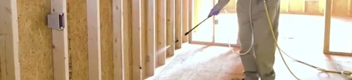 Termite treatment technician applying spray along framing and unfinished walls in Akron, OH